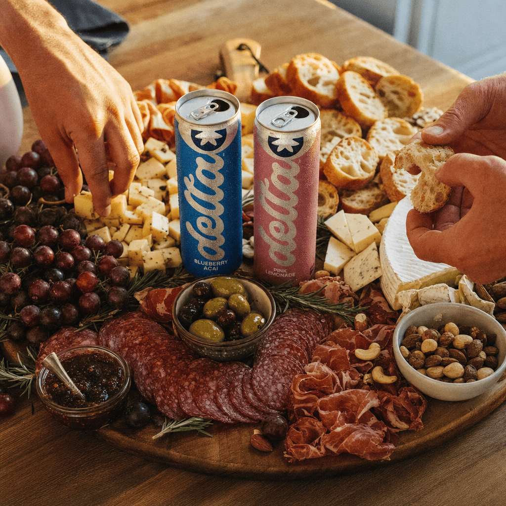 Charcuterie board on a kitchen island at golden hour, two Moderate cans on the board, hands reaching in.