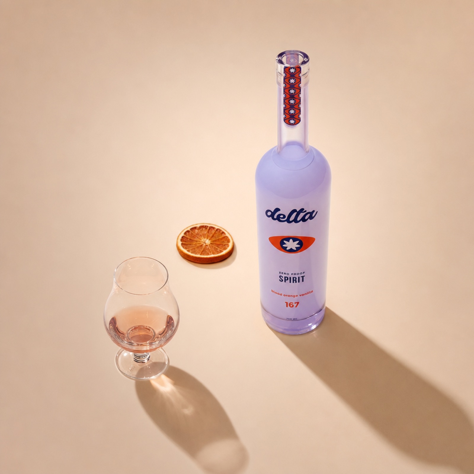 A small snifter holding a neat pour of the Delta Spirit, the bottle alongside with a single dried blood orange slice.