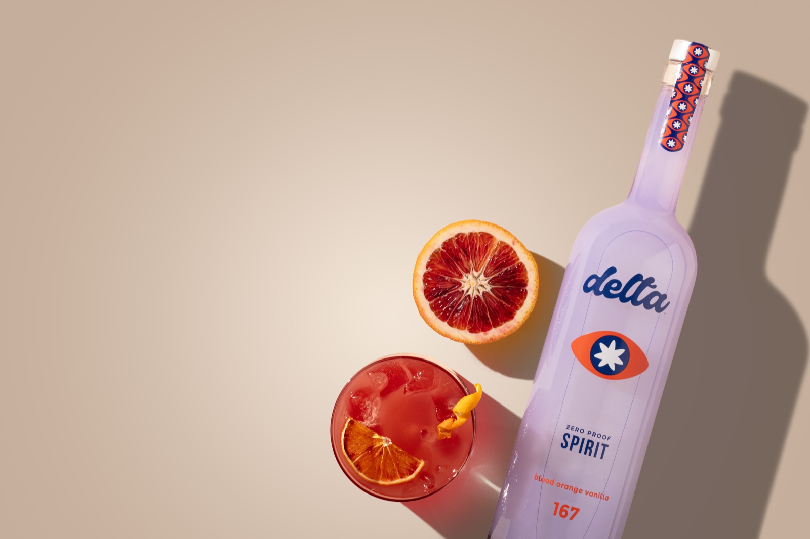A blood orange cocktail in a rocks glass over ice with citrus twist garnish, alongside the Delta Spirit bottle.