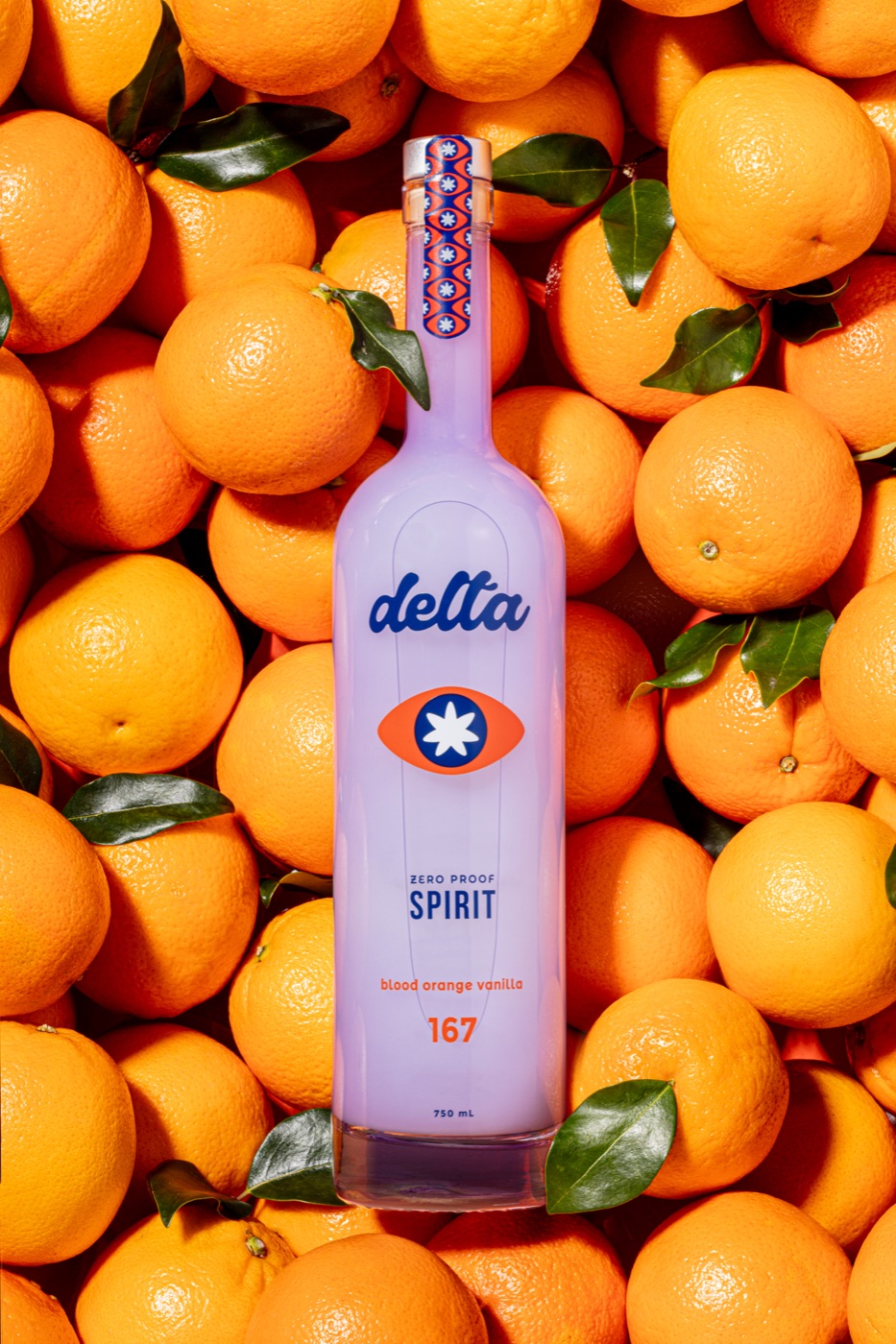 The Delta zero-proof Spirit bottle standing in a bed of fresh blood oranges with leaves still on